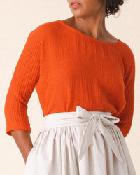 A person wearing Prairie Undergrounds Third Wave in Electric Red, a textured long-sleeve top with a boxy silhouette, paired with a high-waisted, light-colored skirt with a tied belt.
