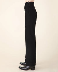 Side view of a person wearing Prairie Underground's Yr Arrow Pant in Black and patterned cowboy boots on a neutral background.