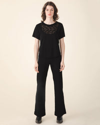 A woman stands wearing a black t-shirt with lace detailing and Prairie Underground Yr Arrow Pant in Black, against a neutral backdrop.