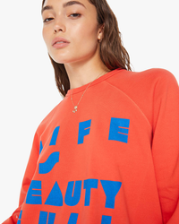 Woman in orange MOTHER DENIM The Biggie Concert in Live is Beauty Full pullover with blue lettering and raglan sleeves.