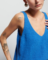 A woman wearing a Nation LTD Cece Sweater Tank in Palace Blue, showcasing her tattoos on her left shoulder and upper arm, stands against a neutral background.