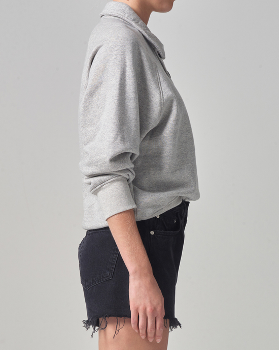Side profile of a person wearing a Phoebe Pullover in Heather Grey made from organic cotton and Citizens of Humanity black denim shorts.