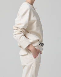 Side profile of a person wearing a cream-colored Citizens of Humanity Sam Sweatshirt in Canvas in an oversized fit with hands in pockets.