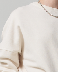 Close-up of a person wearing a plain white Citizens of Humanity Sam Sweatshirt in Canvas with an oversized fit and a silver chain necklace.
