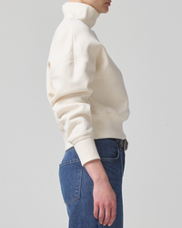 Side profile of a person wearing a Citizens of Humanity Koya Turtleneck in Canvas hoodie and blue jeans.