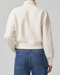 Person wearing a beige Citizens of Humanity Koya Turtleneck sweatshirt and blue jeans viewed from the back.