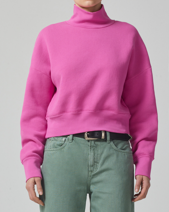 A person wearing a Citizens of Humanity Koya Turtleneck in Rosey and green trousers with a black belt.