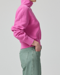 Side view of a person wearing Citizens of Humanity's Koya Turtleneck in Rosey and green pants against a neutral background.