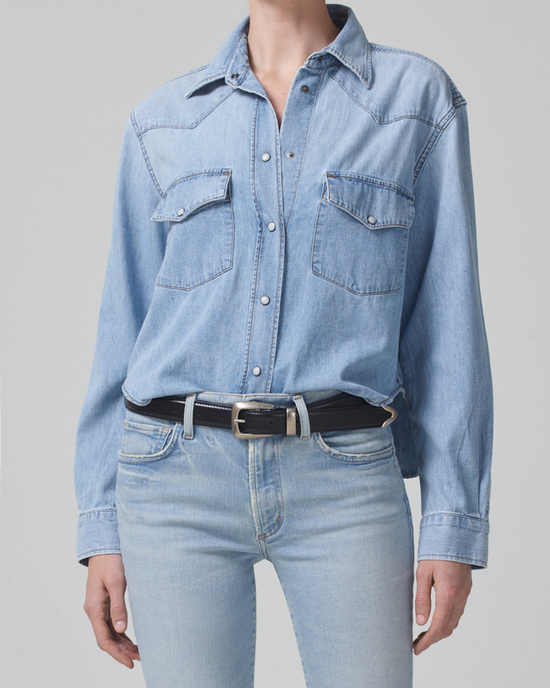 Person wearing a light blue Pharos Cropped Western shirt by Citizens of Humanity and high waist denim jeans with a black belt.
