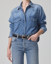 Person wearing a Citizens of Humanity Cropped Western Shirt in Carolina Blue and high waist denim jeans with a black belt.