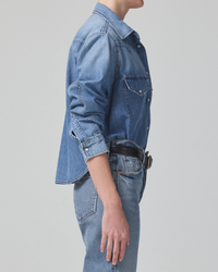 Side profile of a person wearing a Citizens of Humanity Cropped Western Shirt in Carolina Blue jacket and high waist denim jeans with hands by their side.
