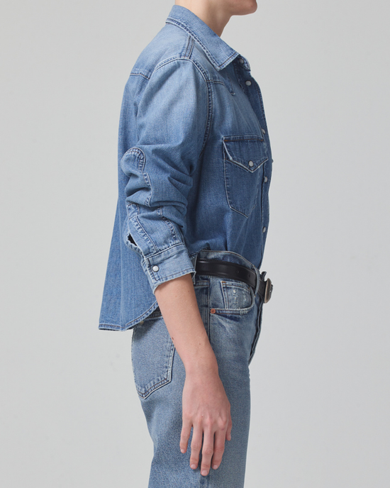 Side profile of a person wearing a Citizens of Humanity Cropped Western Shirt in Carolina Blue jacket and high waist denim jeans with hands by their side.