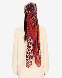 A person seen from behind wears a cream sweater and the Square / Carre 130 Papillons in Red by Inoui Editions, an oversized bandana featuring butterfly and animal prints, tied around their head and draped down their back.