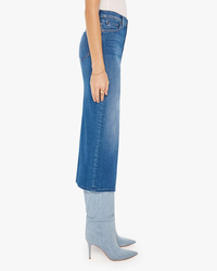 Woman wearing a Mother's The Reverse Pencil Pusher in Hue Are You? denim skirt of midi length and light blue high-heeled boots standing sideways.