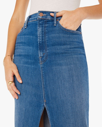 Woman demonstrating a midi-length, high-rise denim skirt by pulling at the waistband of The Reverse Pencil Pusher in Hue Are You? by Mother.