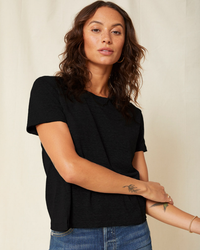 A woman with a tattoo on her forearm wearing an AMO Twist Tee in Black, slightly cropped, and jeans.