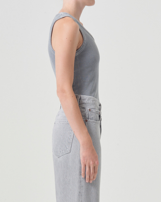 Side profile of a woman wearing an AGOLDE Poppy Scoop Neck Tank in Mirror Ball made from organic cotton and lightweight rib knit, paired with light blue jeans, standing against a white background.