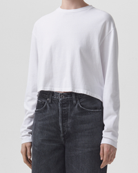 Person wearing an AGOLDE Mason Cropped Tee in White and blue jeans against a neutral background.