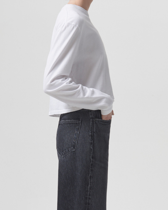 Person wearing an AGOLDE Mason Cropped Tee in White and AGOLDE blue jeans, standing sideways with hand in pocket.