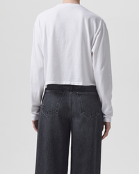 A person standing with their back to the camera, wearing an AGOLDE Mason Cropped Tee in White made from organic cotton and blue denim jeans.