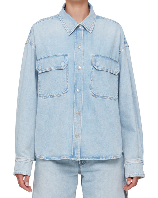 Person wearing an AGOLDE Gwen Slice Shirt in Tension Washed light blue denim, featuring a button-up front and chest pockets made from organic cotton.