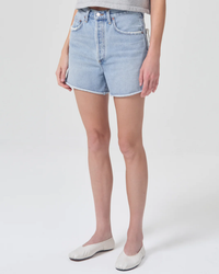 A person standing in light blue high rise AGOLDE Dee Shorts in Hazard paired with white flat shoes.