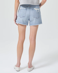 A person standing in white shoes wearing AGOLDE Dee Short in Hazard high rise denim shorts with a frayed hem.