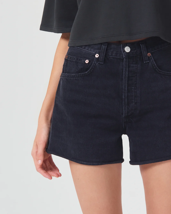 A person showcasing the side pocket and fit of dark high-rise AGOLDE Dee Shorts in Slow Burn.