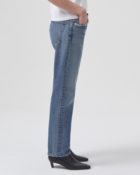 A person wearing AGOLDE's Parker Long straight leg jeans in Invention wash and black heeled shoes standing against a plain background.