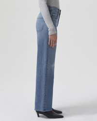 A person standing sideways wearing mid rise Harper Straight Jean in Flash AGOLDE jeans and black boots.