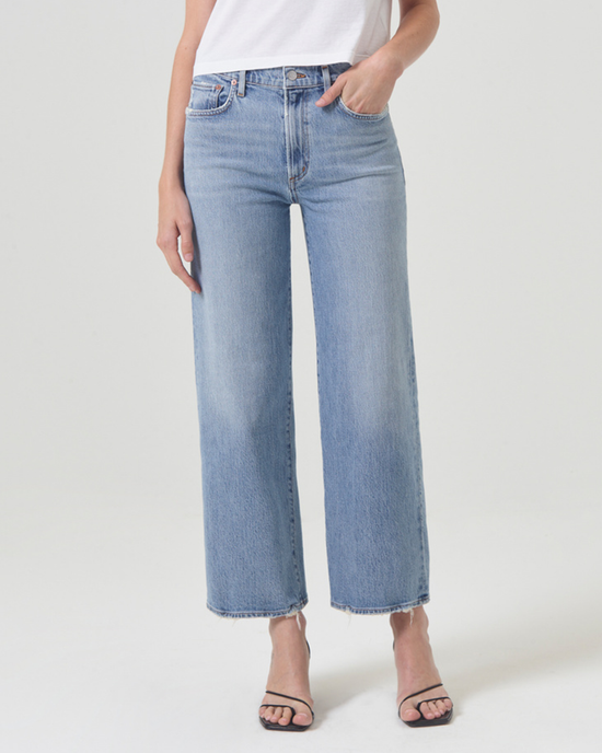 Woman standing wearing blue AGOLDE Harper Straight Crop in Hassle mid-rise straight leg jeans and black sandals.