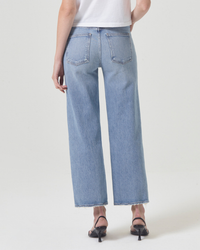 Woman from behind wearing frayed-hem, comfort stretch denim AGOLDE Harper Straight Crop in Hassle mid-rise straight-leg blue jeans and black heels.