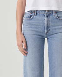Close-up of a person wearing AGOLDE Harper Straight Crop in Hassle blue jeans with a hand resting on the thigh.