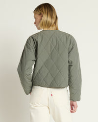 A person with blonde hair, seen from the back, wears the Nation LTD Aspen Quilted Jacket in Castor Grey and high-waisted off-white jeans against a plain light background.