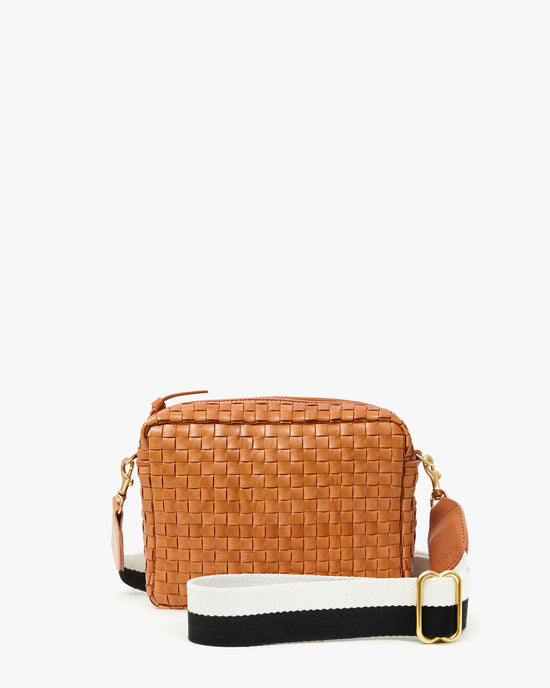 The Clare V. Adj Crossbody Strap in Black & Cream Stripe is featured on a small, rectangular tan woven leather handbag with gold hardware and a gold zipper, shown against a plain white background. The adjustable strap is detachable for versatile styling.