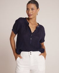A woman wearing a Bella Dahl Short Sleeve Raglan Pullover in Tropic Navy and white pants, standing with hands in pockets and looking to the side.