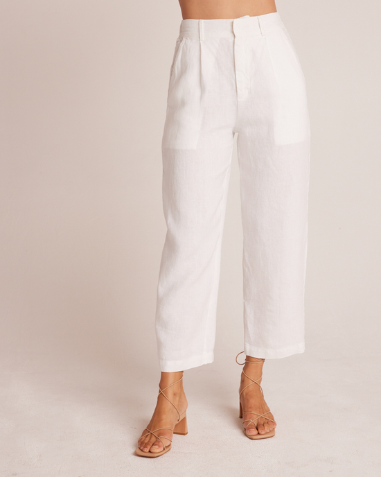 Cropped view of a person wearing Bella Dahl's Relaxed Pleat Front Trouser in White and tan strappy sandals against a beige background.