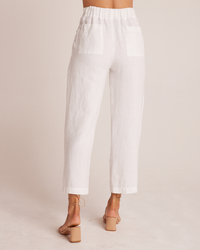 Rear view of a person wearing Bella Dahl's Relaxed Pleat Front Trousers in White and beige high-heeled sandals against a neutral background.