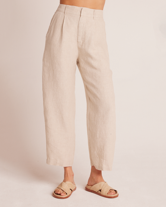 A person wearing a pair of Bella Dahl Relaxed Pleat Front Trousers in Linen Sand.