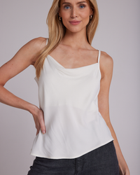Woman posing in a Bella Dahl Cowl Neck Camisol in Winter White with adjustable spaghetti straps and dark pants.