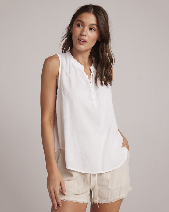 Woman in a casual Bella Dahl Sleeveless Pullover in White with a Mandarin collar, white blouse, and beige shorts.