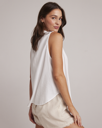 Woman in a Bella Dahl Sleeveless Pullover in White with a Mandarin collar and beige shorts looking over her shoulder.