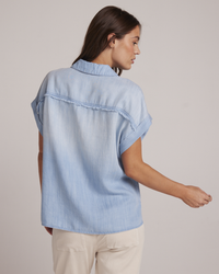 A woman viewed from behind, wearing a Bella Dahl Two Pocket S/S Shirt in Caribbean Wash and beige pants.