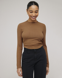 Woman smiling in a Bella Dahl Long Sleeve Crop Crew Neck in Iced Mocha brown ribbed top and black trousers against a neutral background.