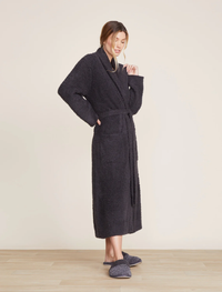 Woman wearing a Barefoot Dreams Cozychic Solid Robe in Carbon and slippers, standing in a neutral-toned room.