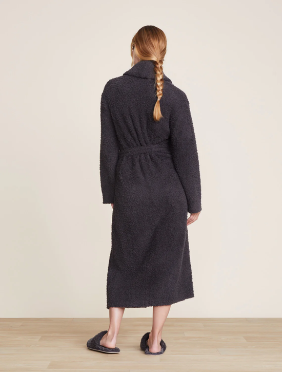 Woman standing with her back to the camera, wearing a Barefoot Dreams Cozychic Solid Robe in Carbon constructed from Polyester Microfiber, featuring a dark hue with a waist tie and slippers, showcasing the back design.