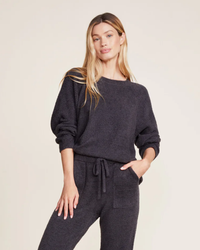 A woman posing in a casual dark grey loungewear set with a Barefoot Dreams CCL Rib Blocked Pullover in Carbon.