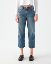 A person wearing AMO's Billie Cropped Wide Straight Leg in Chaperone jeans and black loafers stands against a plain white background. Only the lower half of the body is visible.
