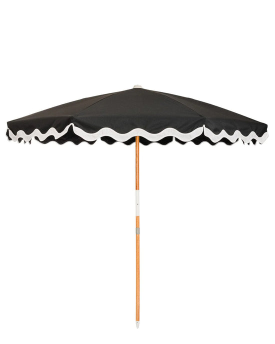 The Amalfi Umbrella - Rivie Black by Business & Pleasure Co features a black UV water-resistant canopy with white scalloped trim and a wooden pole, shown fully open against a plain white background.