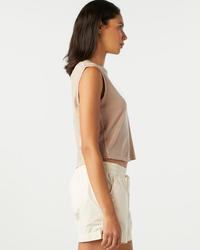 Side view of a woman in a Sleeveless Babe Tee by AMO and AMO denim shorts standing against a plain background.